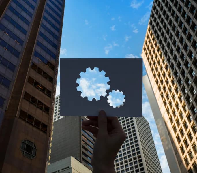Hand holding a card with gears between office buildings